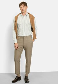 Leicht gestreiftes Button-Down-Hemd in hellgrün und weiß; brauner Pullover lässig über die Schultern drapiert; beige Hose; dunkelbraune Schuhe; braune Socken.