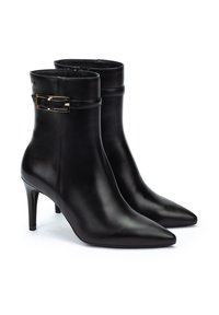 Botas de cuero negro hasta el tobillo con punta afilada y tacón de aguja. Presentan un detalle de hebilla dorada en el lado exterior.