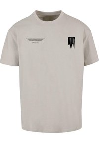 Helle graue Baumwoll-T-Shirt mit Rundhalsausschnitt, das mit schwarzem Text horizontal über die Brust bedruckt ist und einem Logo auf dem linken Ärmel.