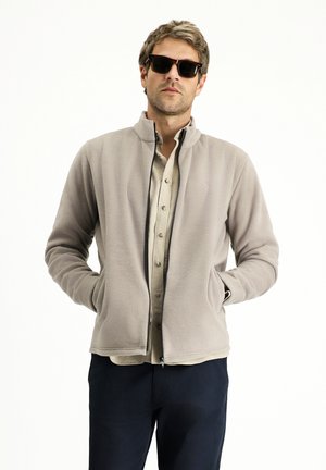 Light gray fleece jacket with standing collar, zip closure, and side pockets. Worn over a beige button-up shirt and dark pants.