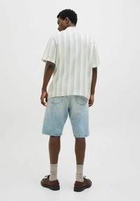 Chemise à manches courtes rayée dans des couleurs claires, associée à un short en denim bleu clair. Des chaussures brunes et des chaussettes beiges complètent le look.