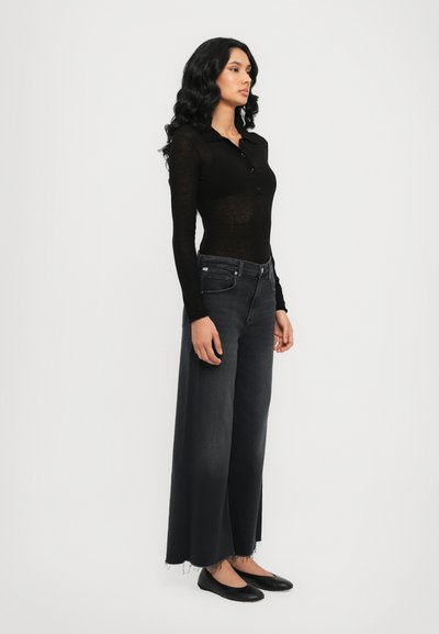 Haut noir à manches longues avec des boutons, associé à un jean large gris foncé avec des ourlets effilochés et des ballerines noires. Design minimaliste.
