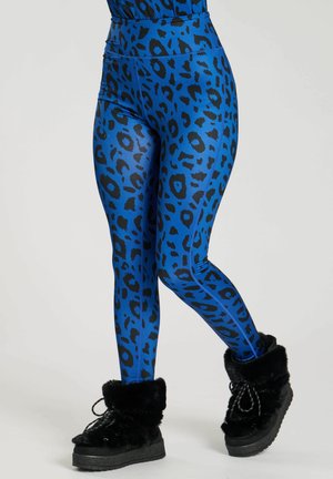 Blauwe leggings met luipaardprint en zwarte vlekken, met een hoogtaille ontwerp en een glanzende textuur. Gecombineerd met zwarte, met bont gevoerde enkellaarzen.