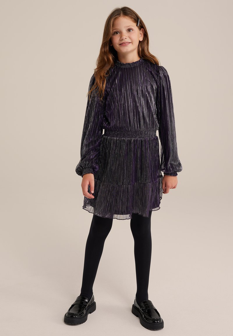 Lila plisserad klänning med långa ärmar, elastisk midja och lager-på-lager kjol. Bärs med svarta strumpbyxor och klumpiga svarta skor. Slät, blank textur.