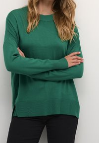 Zielony sweter z dzianiny z okrągłym dekoltem o ribbrowanym wykończeniu, obniżonymi ramionami oraz bocznymi rozcięciami na dole. Gładka tekstura i luźny krój.
