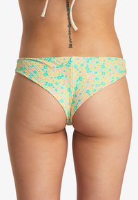Bas de bikini coloré avec un motif floral, présentant une base jaune pastel ornée d'accents turquoise et rose, avec un tissu froncé sur les côtés.