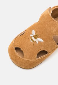 Beige semskede sandaler med utskårne detaljer og en brodert bie-design foran. Myk tekstur med polstret innside.