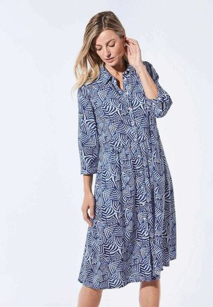 Robe à motifs bleus et blancs avec un col, des manches trois quarts et une coupe ample. Présente des motifs géométriques sur l'ensemble du tissu.