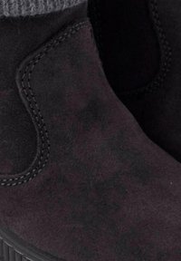 Botas de tobillo de ante negro con suela de goma gruesa, que presentan un puño de punto gris texturizado y detalles de costura a lo largo de los bordes.