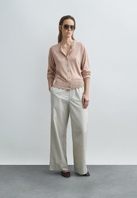 Light pink cardigan with buttons, paired with wide-leg beige pants featuring a pinstripe pattern. Brown flat shoes and dark sunglasses.