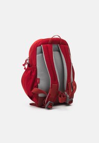 Red backpack with gray mesh padding on the straps, adjustable buckles, and a side pocket. Rounded shape with soft fabric texture.