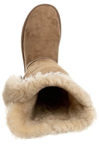 Brązowy zamszowy but z miękką kremową futrzaną wyściółką i założonym na zewnątrz mankietem, charakteryzujący się gładką powierzchnią zewnętrzną i zaokrąglonym kształtem palców.