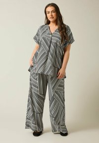 Completo coordinato a righe bianco e nero composto da una maglietta larga a maniche corte con un bottone e pantaloni larghi con motivi geometrici.