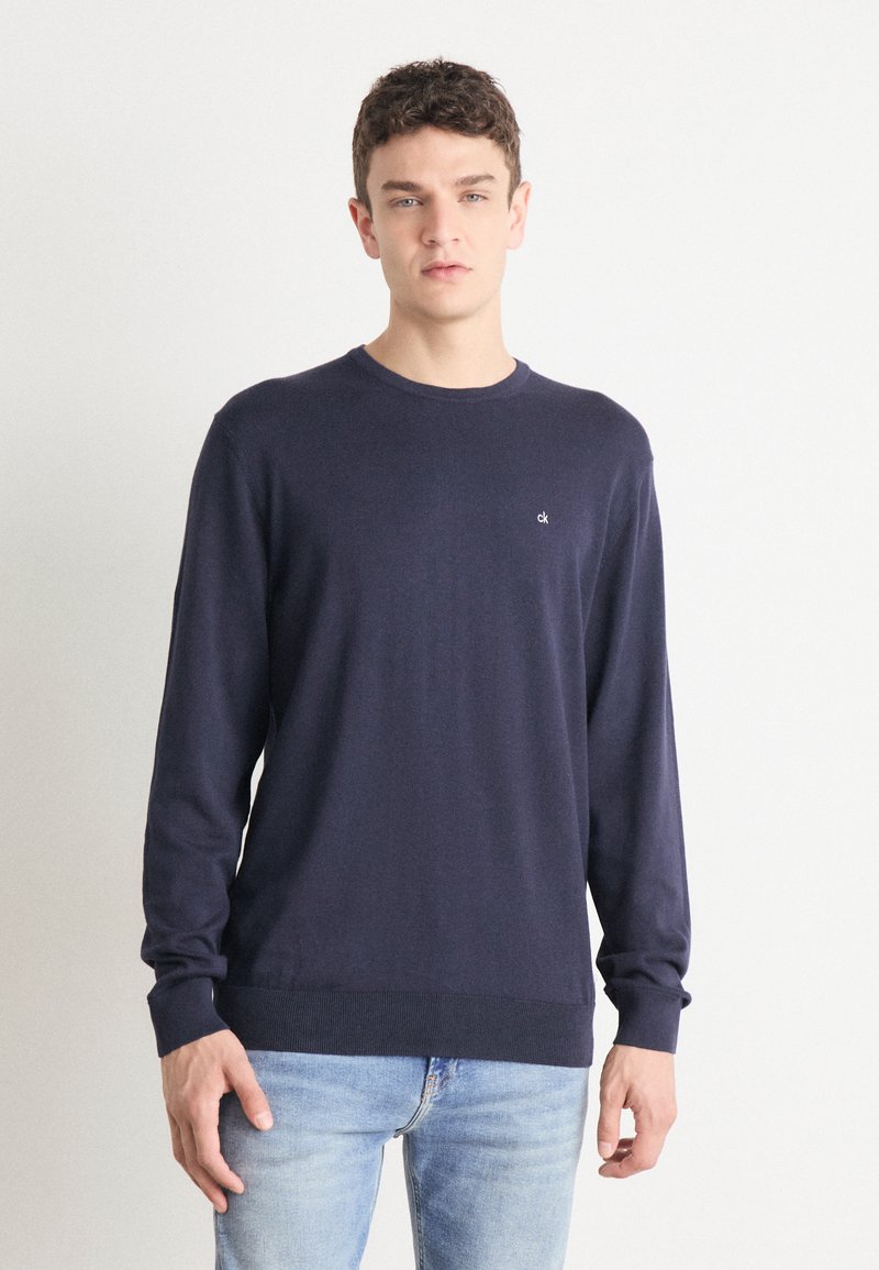 Tamsiai mėlynas apvalios kaklo megztinis su ilgomis rankovėmis, pagamintas iš minkštos medžiagos. Pasižymi mažu logo ant krūtinės ir rausvomis rankogaliais bei apatine dalimi.