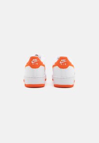 Nike Air tenisice imaju gornji dio od bijele kože s narančastim naglascima na peti i potplatu. Teksturirani gumeni potplat osigurava prianjanje.