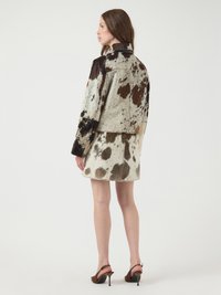 Veste en peau de vache brun et blanc, courte, avec un col, associée à une jupe assortie. Fini texturé et silhouette ajustée.