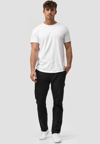 White crew-neck t-shirt paired with black cargo pants featuring side pockets. Model is wearing white sneakers. Casual fit and plain design.