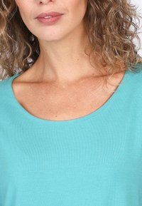 Türkiser, kurzärmeliger Oberteil mit rundem Halsausschnitt, aus glattem Stoff gefertigt. Besitzt ein figurnahes Design und minimale Nähdetails.