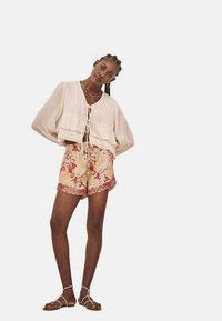 Top recortado de color beige claro con un dobladillo con volantes y un lazo en el frente, combinado con pantalones cortos de colores con un intrincado diseño floral.