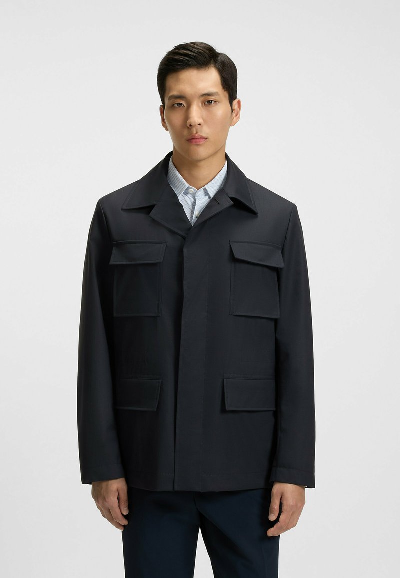 Chaqueta azul marino con tapeta frontal, dos bolsillos en el pecho y cuello con solapa. Fabricada en tela suave con mangas rectas.