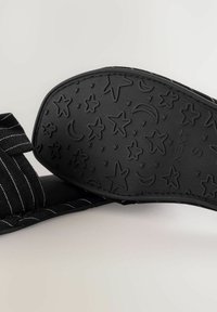 Black sandal with a textured rubber sole featuring star and moon patterns. Fabric straps have a white pinstripe design.