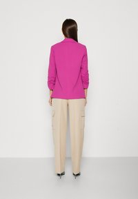 Fuchsia blazer med skräddarsydd passform, slagkrage och rynkade ärmar, tillsammans med beiga cargobyxor med sidofickor.