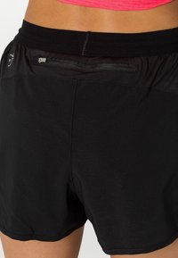 Svarta atletiska shorts med en slät textur, med en flexibel midja och en liten dragkedjeficka bak.