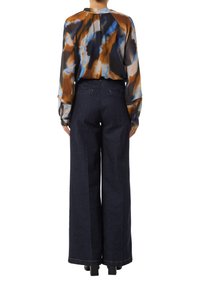 Bunt gemusterte Bluse mit lockerer Passform und langen Ärmeln, ergänzt durch hochgekrempelte, dunkelblaue, weite Jeanshosen.