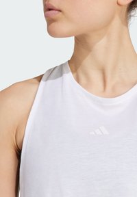 Débardeur de sport blanc avec un col rond et une conception sans manches. Présente un logo blanc discret sur la poitrine. Tissu lisse et léger.