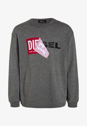 Szara bluza Diesel z czarnym napisem i czerwonym naszywką częściowo zakryta przez złożony różowy kwadrat z tkaniny na piersi.