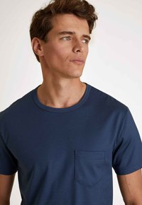 Dunkelblaues T-Shirt mit kurzen Ärmeln aus geripptem Stoff, mit rundem Ausschnitt und einer Brusttasche auf der linken Seite.