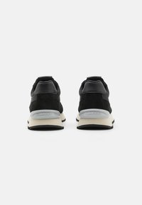 Baskets en suède et cuir noirs avec une semelle en caoutchouc crème, présentant un renfort de talon gris et un design minimaliste, présentées de dos.