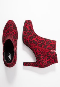Bottines à imprimé léopard rouge et noir, avec un bout pointu, une fermeture éclair et un talon haut et épais. Matière douce et texturée.