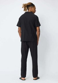 Chemise noire à manches courtes et pantalon assorti en coupe décontractée, fabriqués dans un matériau léger. Design simple sans motifs ni accessoires visibles.