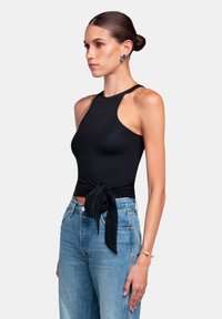 Top negro sin mangas con un escote alto, que presenta un lazo en la cintura. Combinado con jeans de tiro alto de color azul claro. Textura suave.
