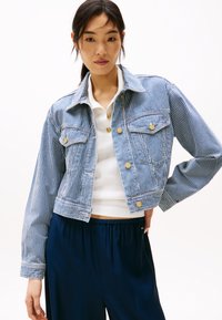 Stripet denimjakke med en kort design, som har gullknapper, frontlommer og en sydd hem, kombinert med en hvit topp og marineblå bukser.