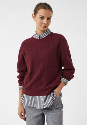 Burgunderfarbener Strickpullover mit Rundhalsausschnitt, ausgestattet mit geripptem Texture und umgeschlagenen Ärmeln, über einem grau-weißen gestreiften Hemd getragen.