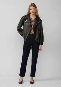 Czarna skórzana kurtka motocyklowa z srebrnymi detalami, top w panterkę, ciemne proste dżinsy oraz czarne buty na niskim obcasie.