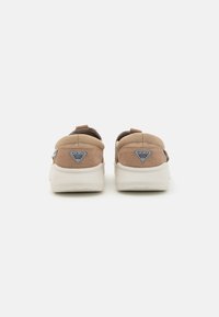 Brązowe zamszowe sneakersy o zaokrąglonym kształcie, z kontrastującą białą podeszwą i akcentami logo na pięcie. Teksturowana cholewka i wyściełany kołnierz.