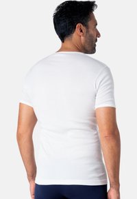 T-shirt blanc à manches courtes en tissu doux, avec un col rond classique et une coupe ajustée. Texture lisse sans motifs visibles.