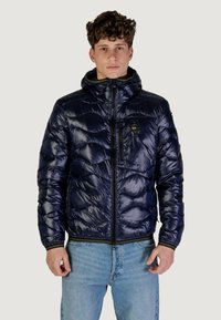 Giubbotto imbottito di un blu scuro, con chiusura a zip frontale, cappuccio e motivo testurizzato. Include una tasca sul petto e dettagli gialli sulla zip.