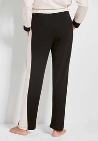 Zwarte en crèmekleurige sportbroek met een tapered fit, elastische tailleband en zijkanten met contrasterende strepen. Zachte stoftextuur.