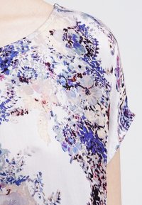 Blommig blus med ett lätt och mjukt tyg i pastellfärger av blått, lila och vitt samt korta ärmar.