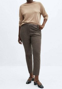 Beige trui, mouwen tot halverwege de armen, gecombineerd met bruin gestreepte broek, slim fit, en zwarte blokhakken.