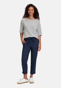 Top a maniche larghe a righe bianche e blu navy, abbinato a pantaloni blu navy con cordino e sneaker bianche. I tessuti dei vestiti sembrano leggeri e rilassati.