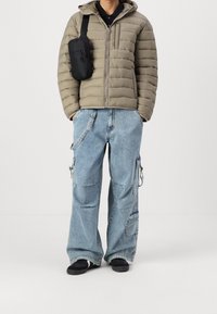 Olivově zelená prošívaná bunda s horizontálním prošíváním, černá crossbody kabelka, světle modré široké cargo džíny s patchworkem a kapsami.