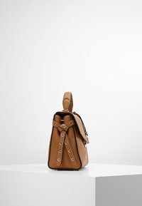 Sac en cuir marron avec une finition texturée, forme conique, bandoulière réglable avec une quincaillerie circulaire, et une poignée sur le dessus pour le transport.
