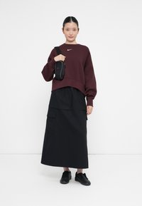 Μαρόν κοντό φούτερ, μαύρη μακριά φούστα και μαύρα αθλητικά παπούτσια. Αξεσουάρ: μικρή μαύρη τσάντα με λουράκι. Απλός σχεδιασμός και μινιμαλιστικά χρώματα.