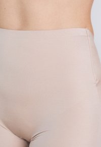 Leggings bej cu talie înaltă, realizate dintr-un material neted și elastic, cu un design fără cusături și o strălucire subtilă, având o ajustare strânsă în jurul taliei.