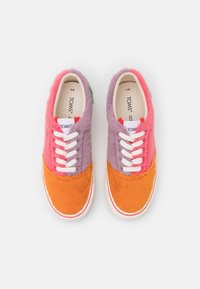 Kolorowe sneakersy TOMS z fioletowym, różowym i pomarańczowym puszystym materiałem, białymi sznurowadłami oraz gumową podeszwą z czerwoną tasiemką.